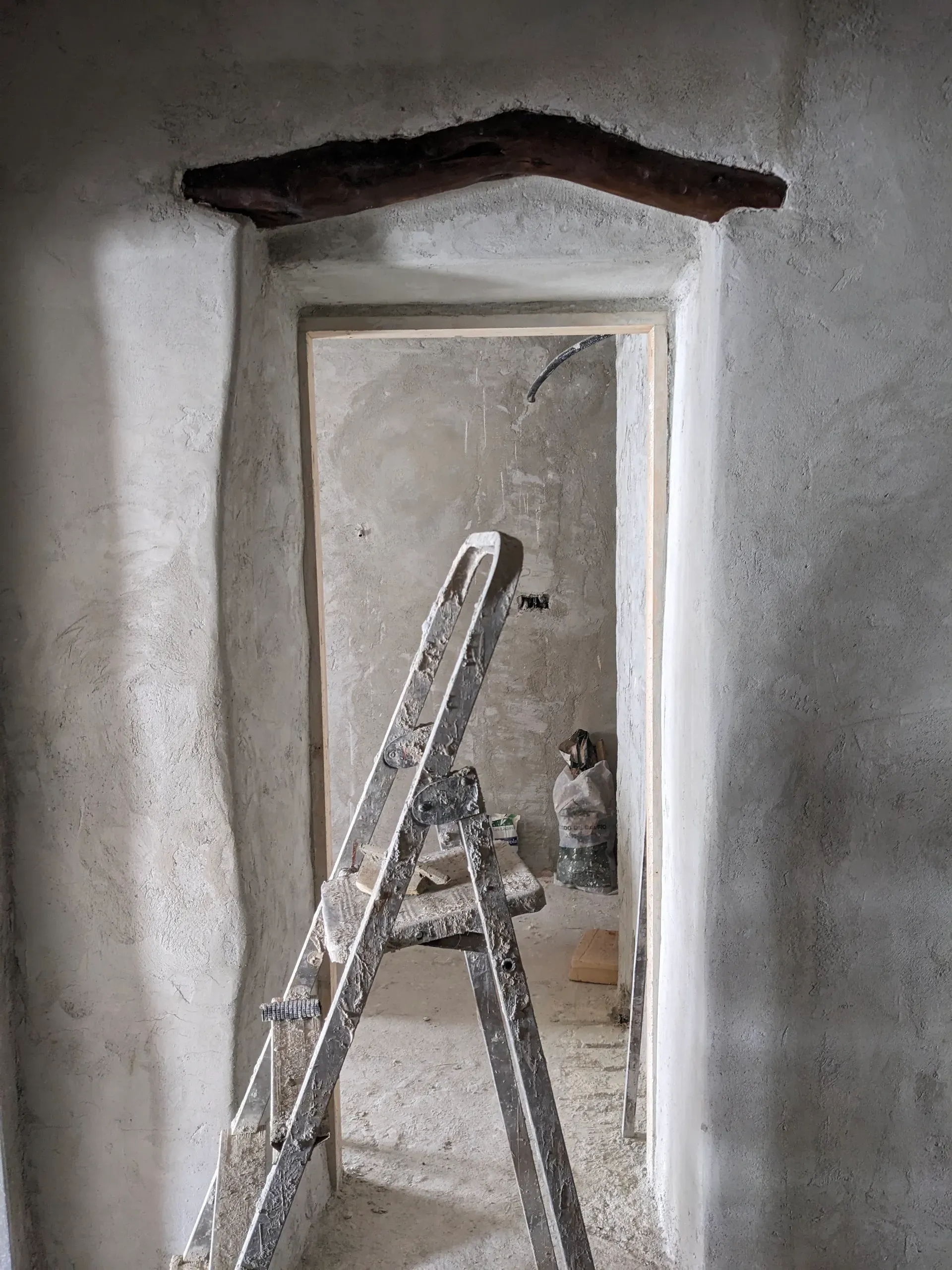 Vista de una estancia en obra a través de un vano de puerta, con viga de madera empotrada.