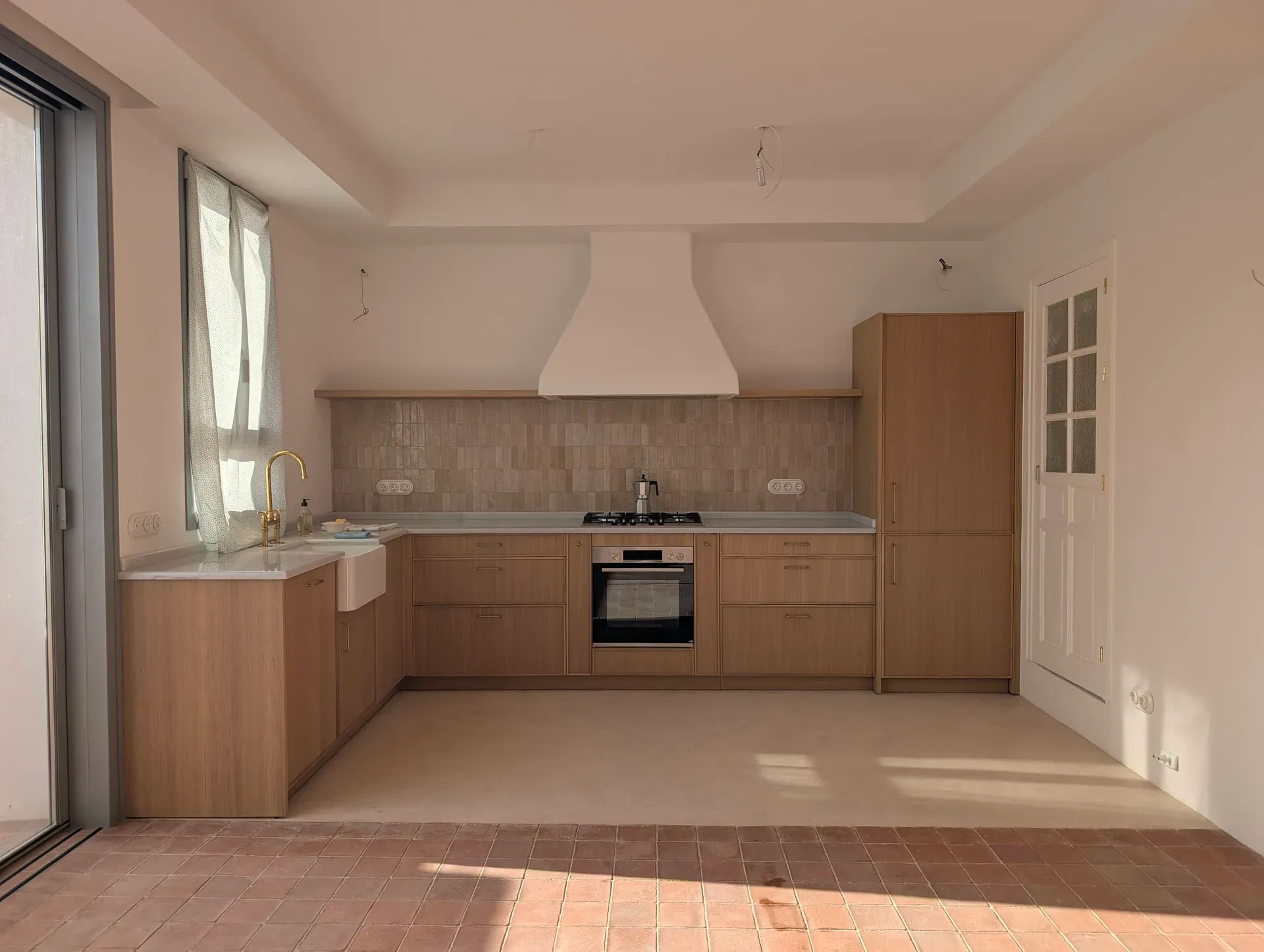 Cocina rehabilitada con suelo continuo de trabadillo y mobiliario de madera, en contraste con pavimento de barro