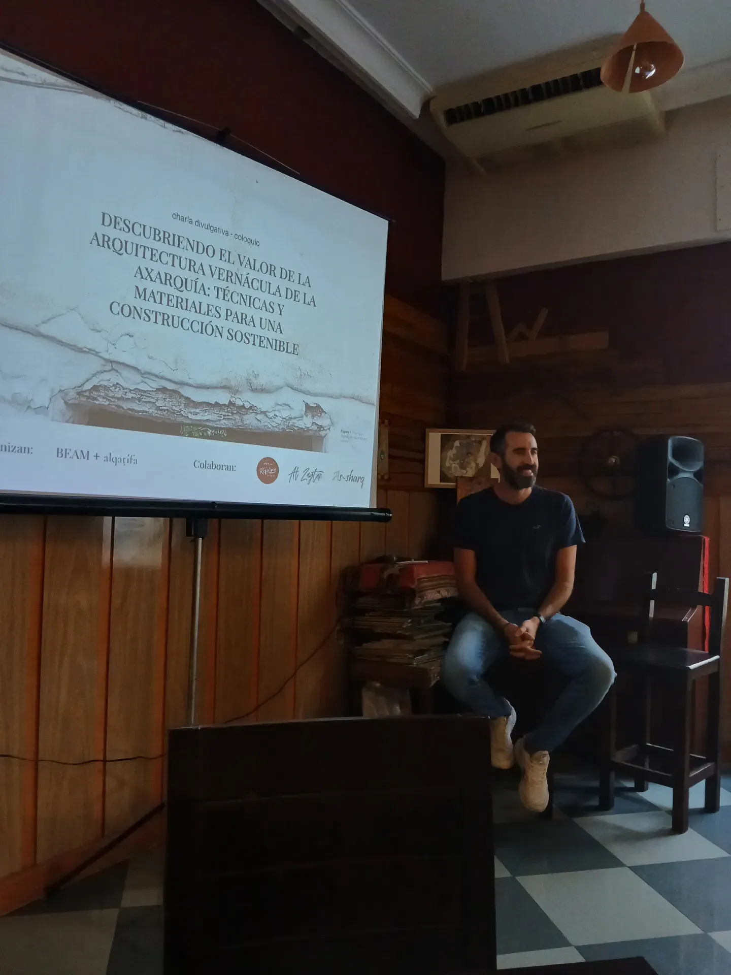 Jesús sentado frente a una pantalla de proyección con el título de la charla sobre arquitectura vernácula de la Axarquía