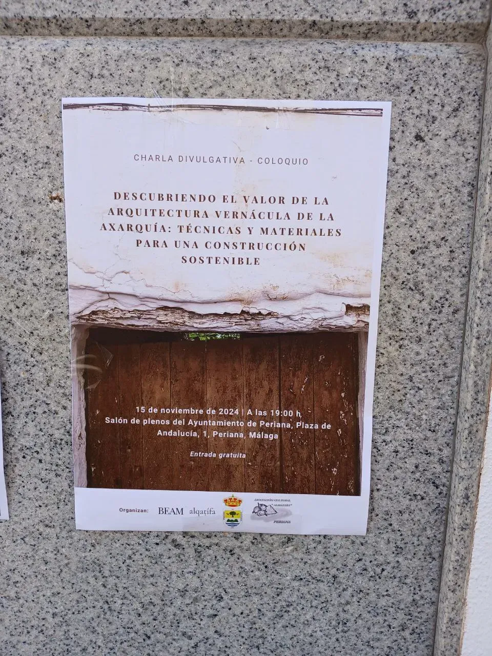 Cartel de la charla divulgativa "Descubriendo el valor de la arquitectura vernácula de la Axarquía" pegado en un muro