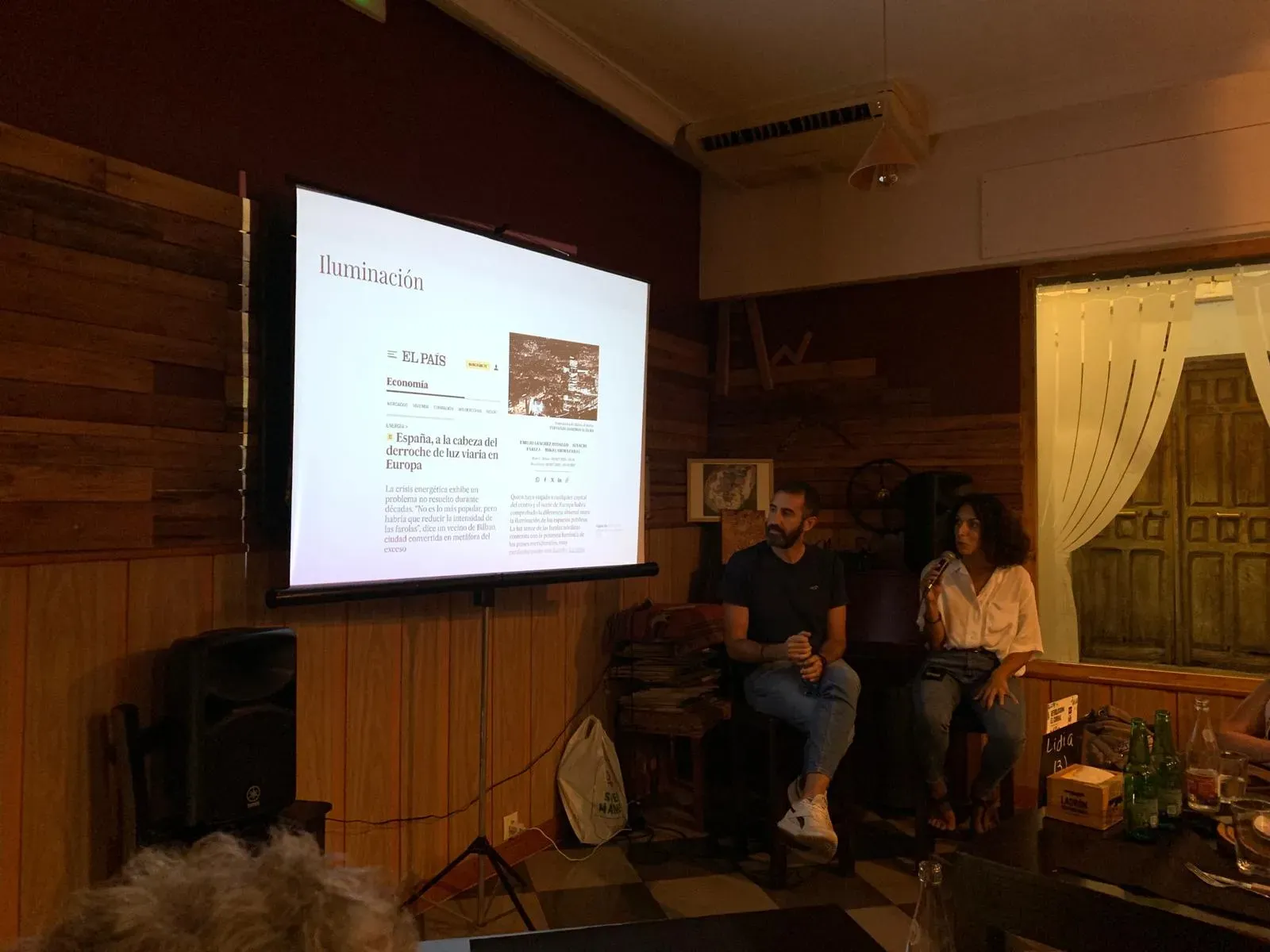 Pantalla de proyección mostrando un artículo sobre derroche de luz viaria durante la conferencia de Jesús y María José