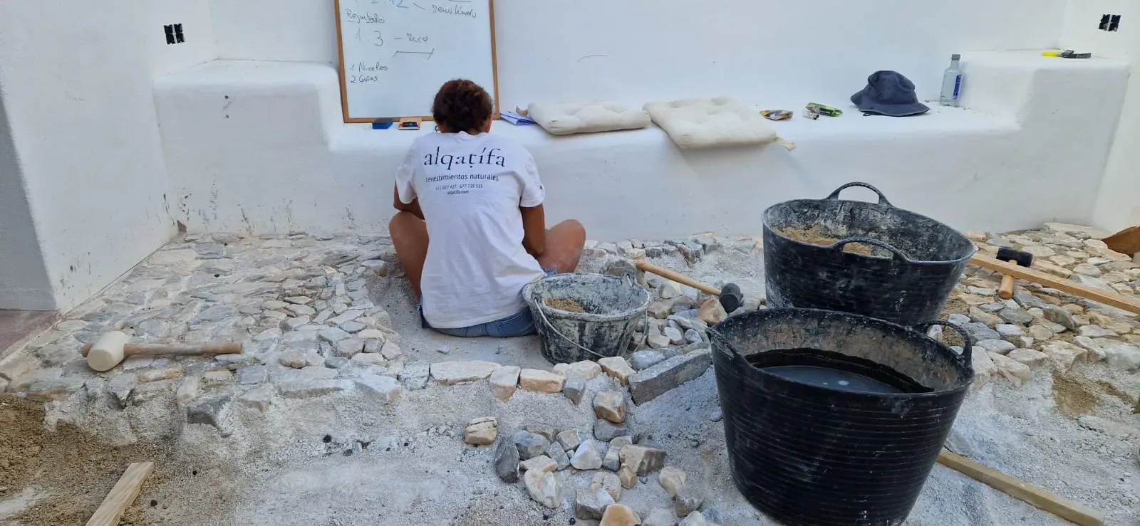 Sesión práctica de empedrado: alumna trabajando la colocación de la piedra bajo la pizarra con indicaciones