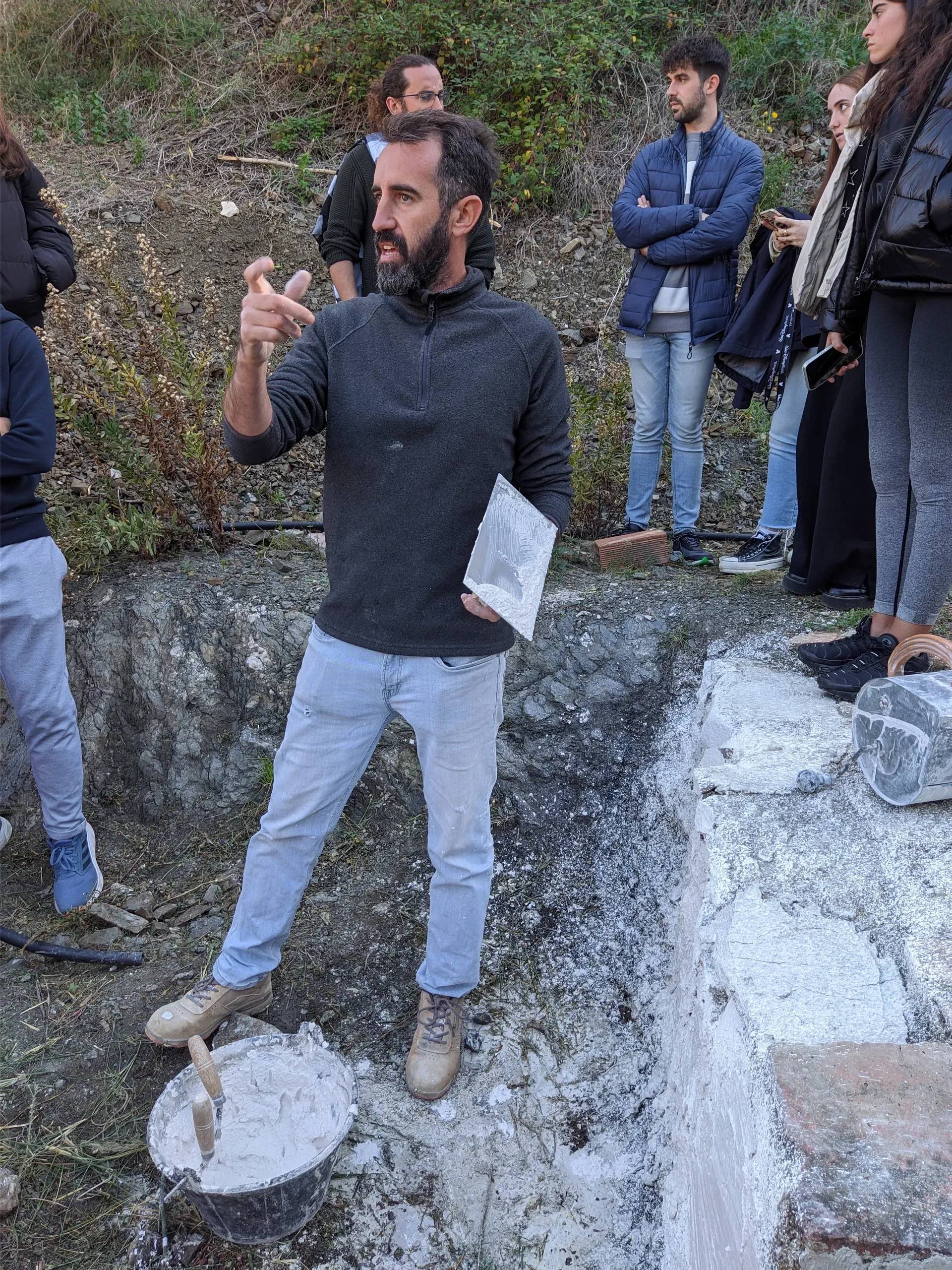 Jesús explicando las propiedades de la cal en pasta con herramientas manuales frente a alumnos