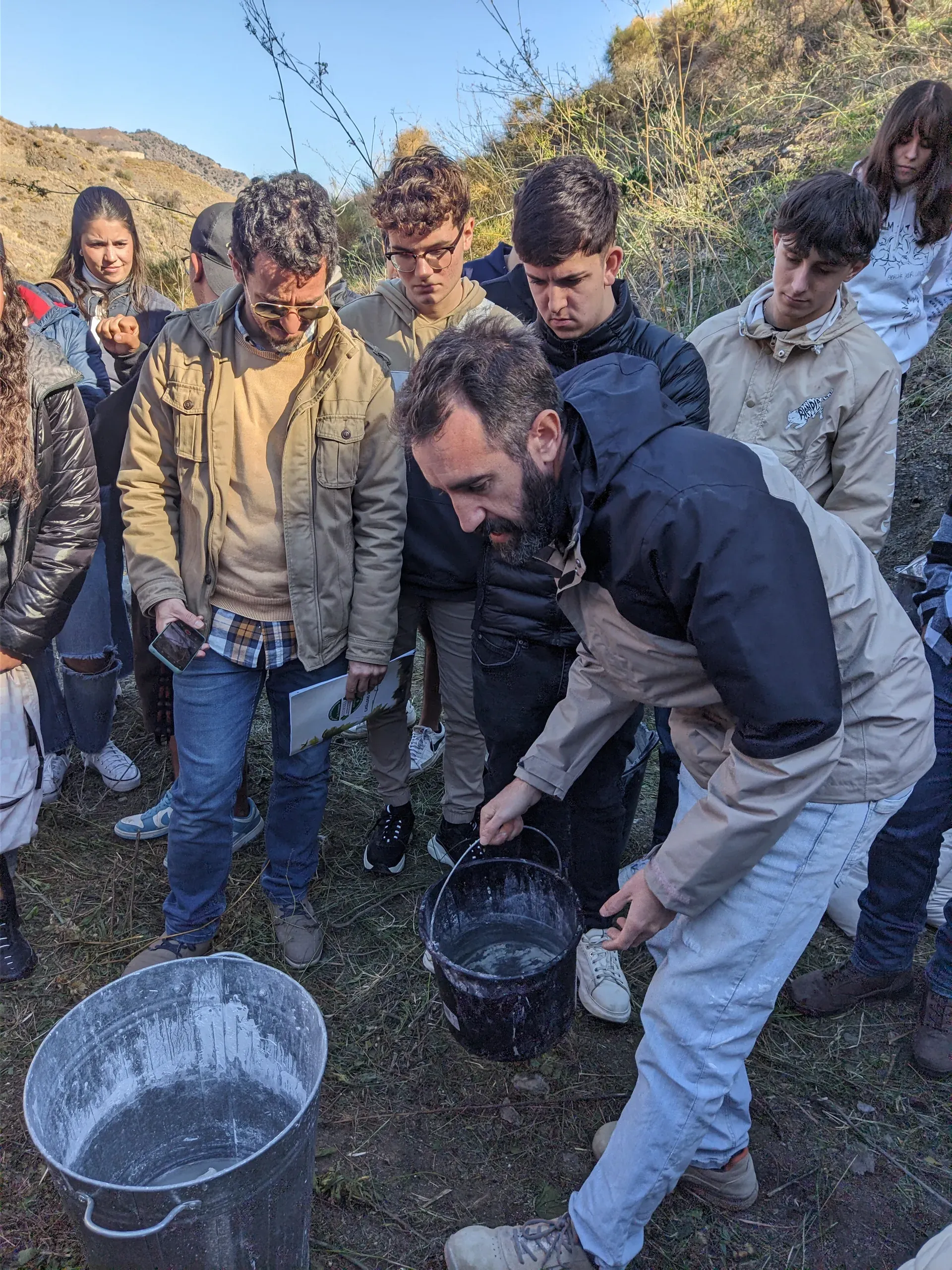 Demostración técnica: Jesús preparando agua de cal rodeado de estudiantes en el campo