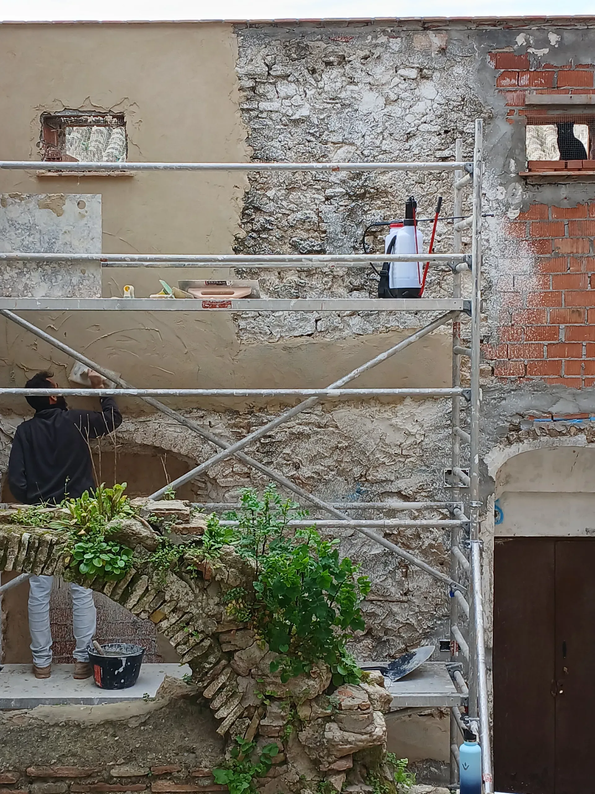 Andamio frente a muro histórico en proceso de restauración, combinando mampostería original con nuevo revoco de cal