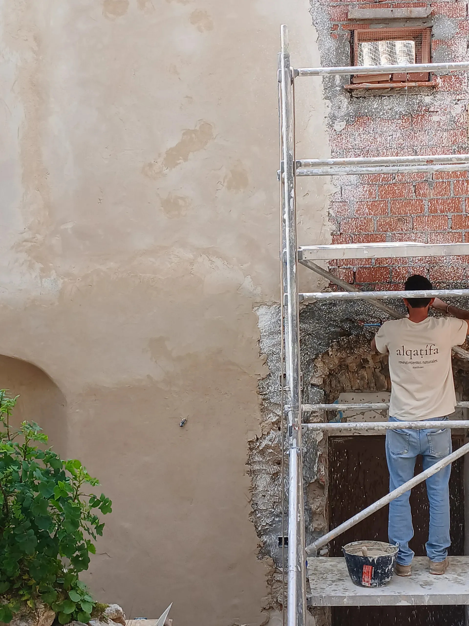 Artesano aplicando mortero de cal sobre muro de ladrillo y piedra desde andamiaje