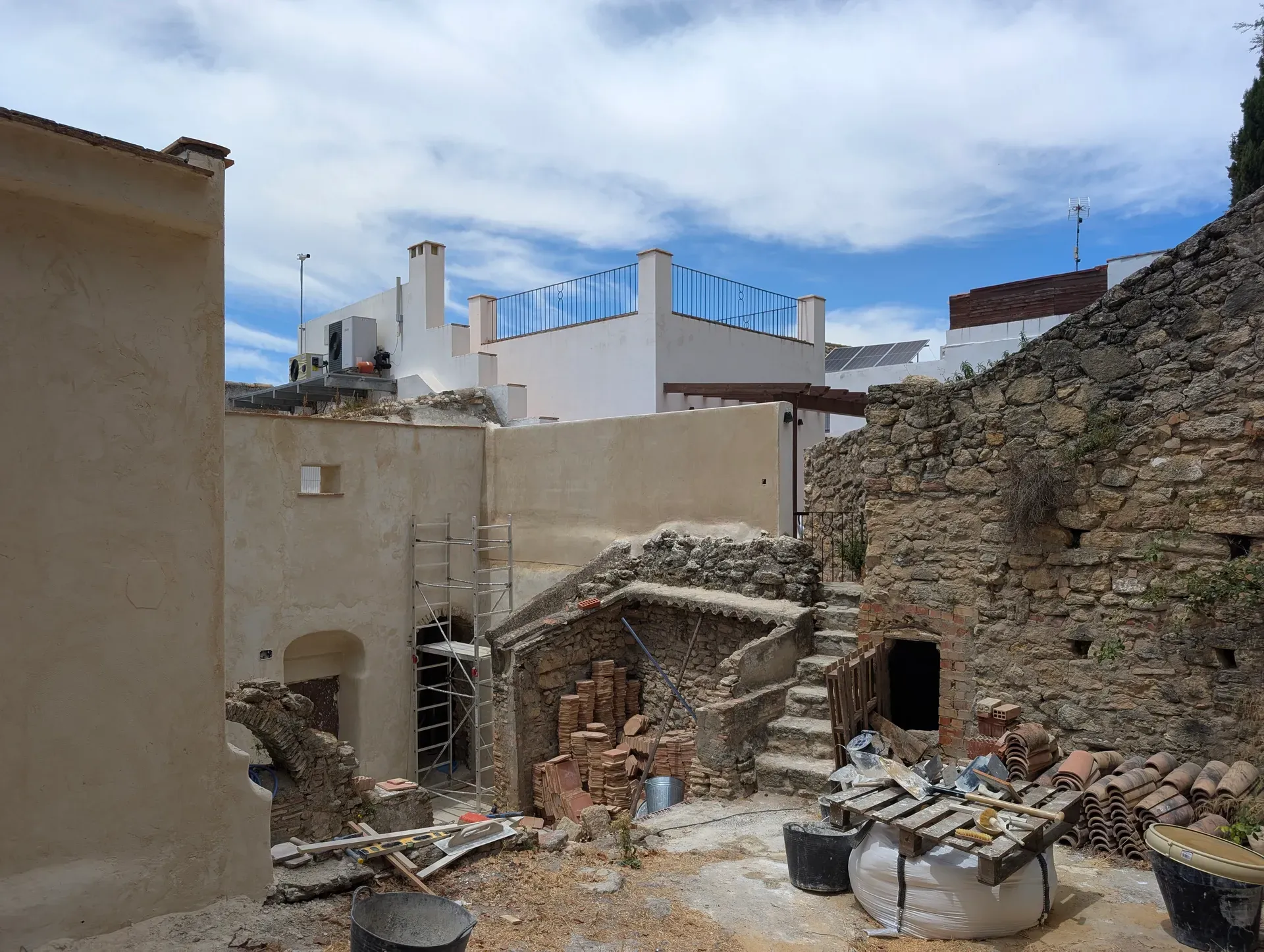 Vista general del patio con volúmenes arquitectura vernácula, muros encalados y restos de mampostería bajo cielo azul