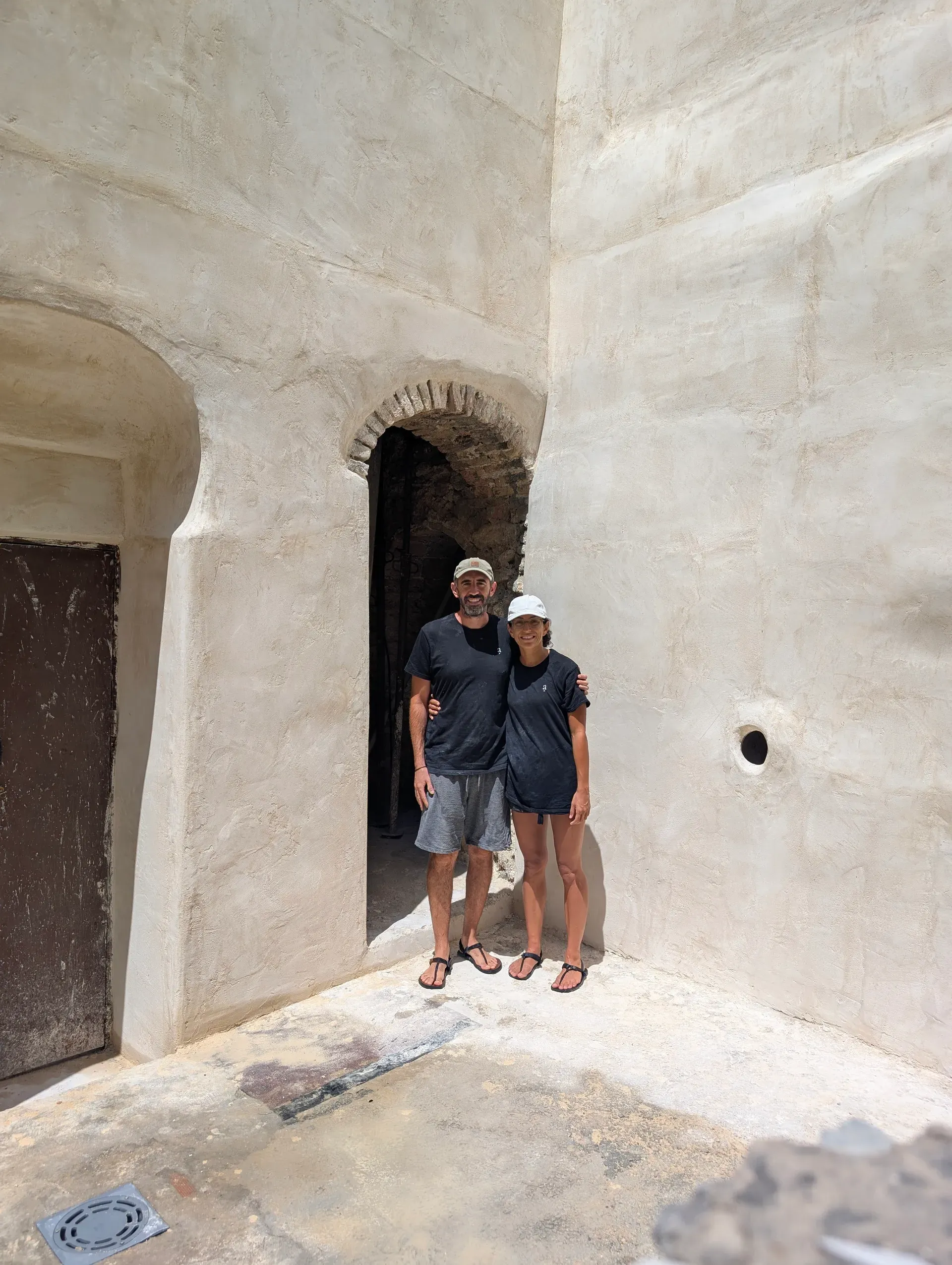 Artesanos posando bajo arco de piedra restaurado en muro de cal, mostrando la escala de la intervención
