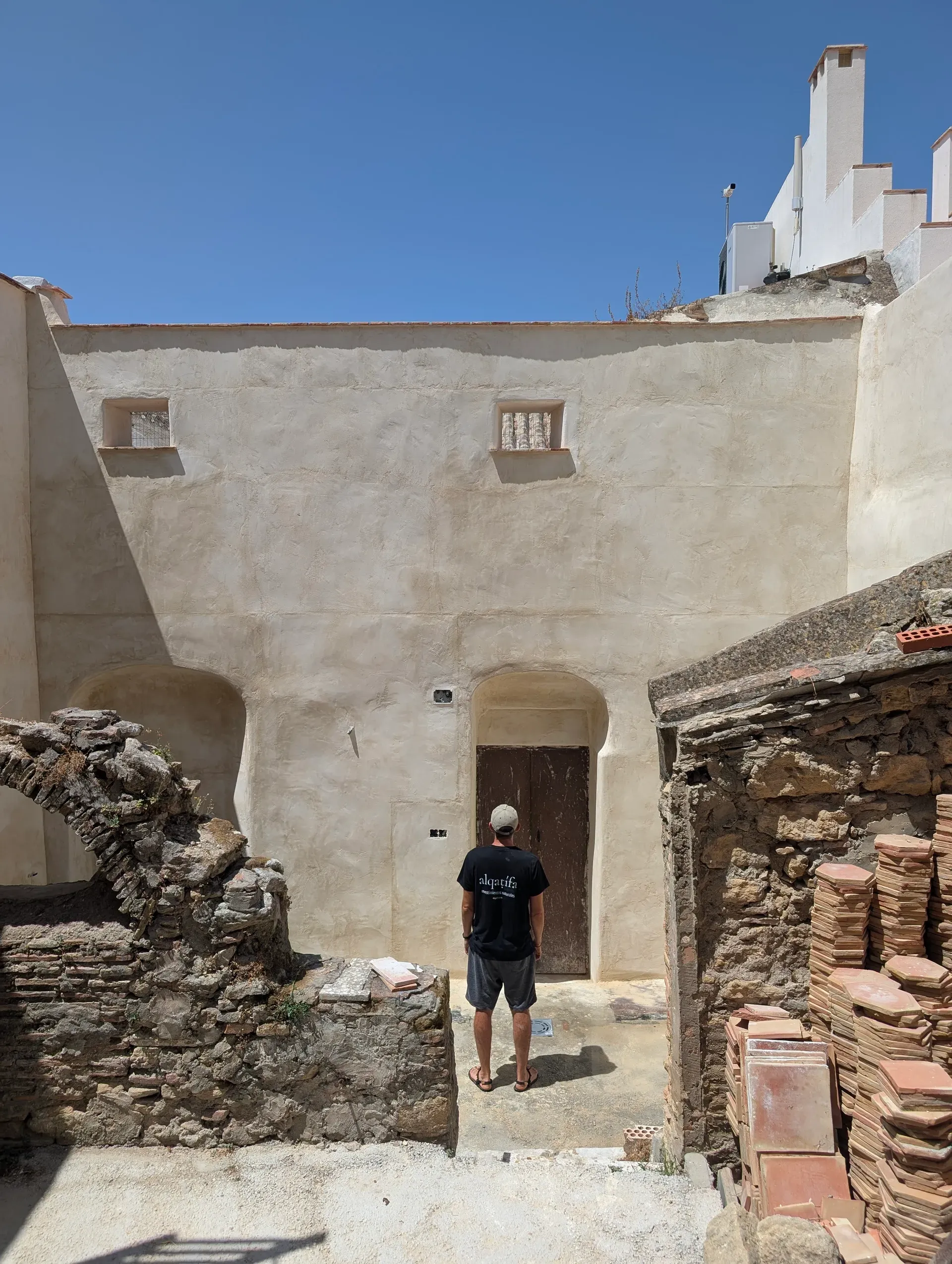 Perspectiva del patio interior con muros de cal texturizados y puerta de madera antigua, contrastando con ruinas de piedra