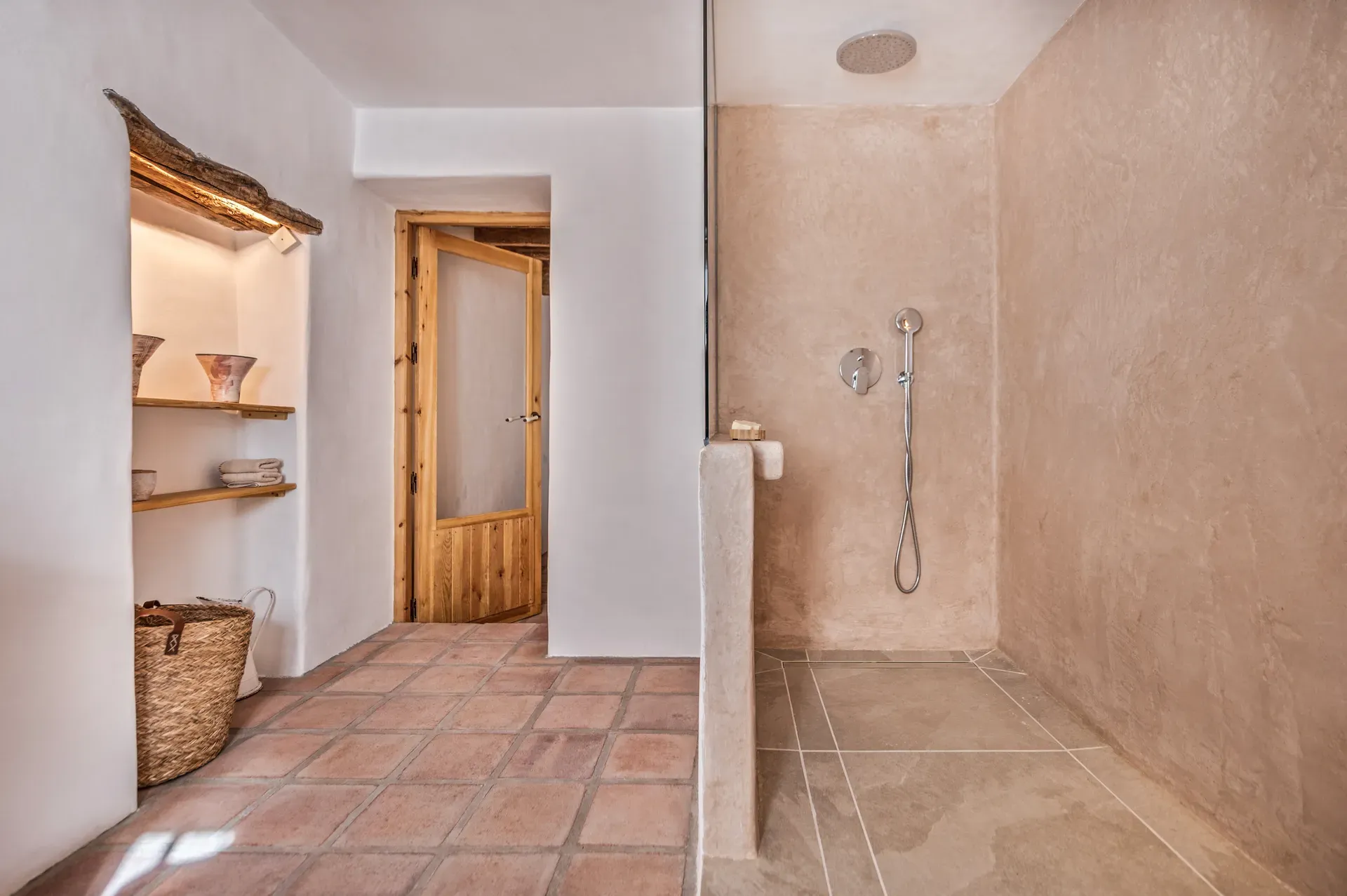 Baño con ducha de tadelakt beige y suelo de terracota, combinando texturas artesanales y diseño rústico contemporáneo