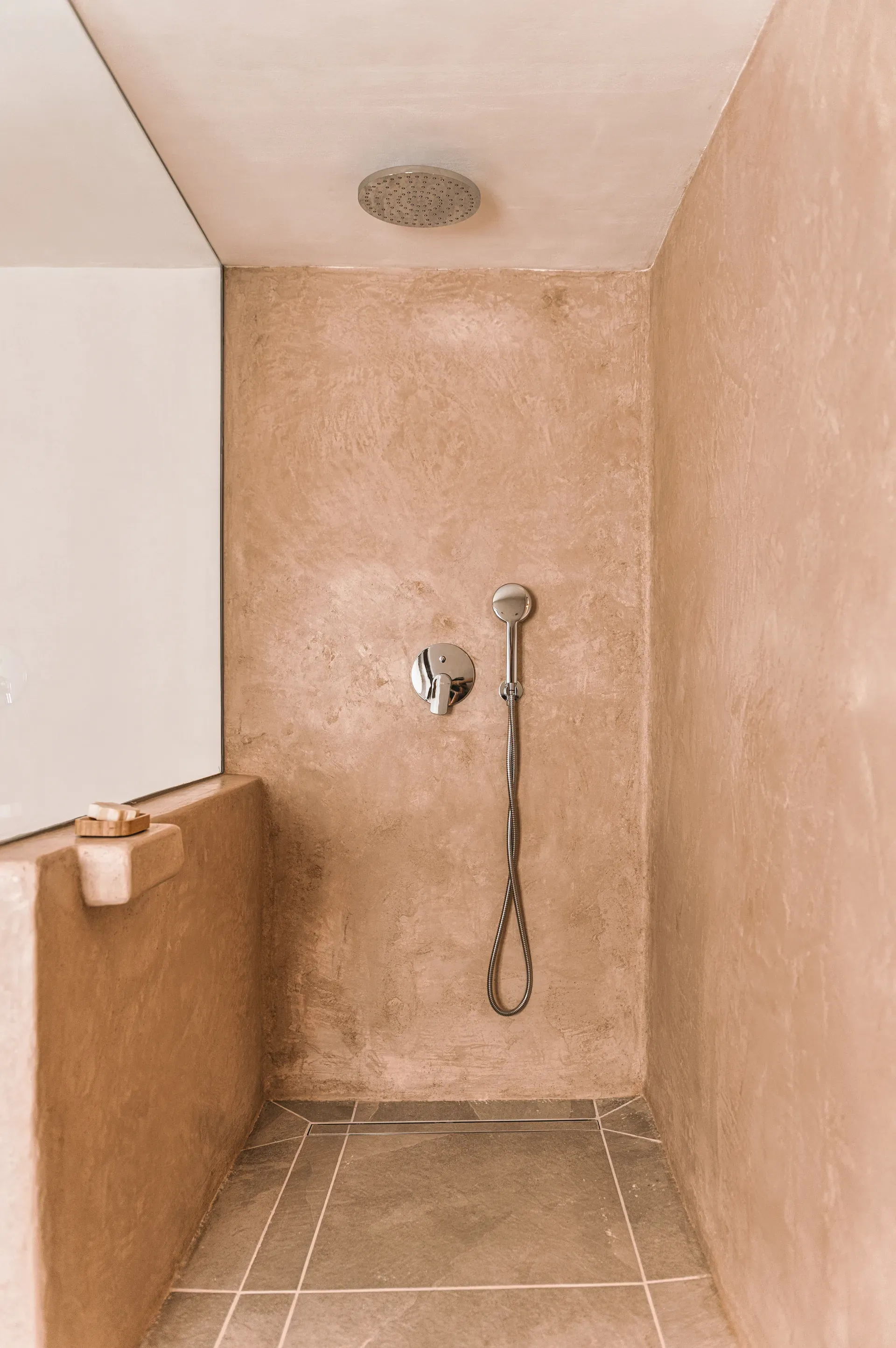 Grifería cromada sobre revestimiento continuo de tadelakt arena, resaltando la textura mineral y las aguas del acabado artesanal