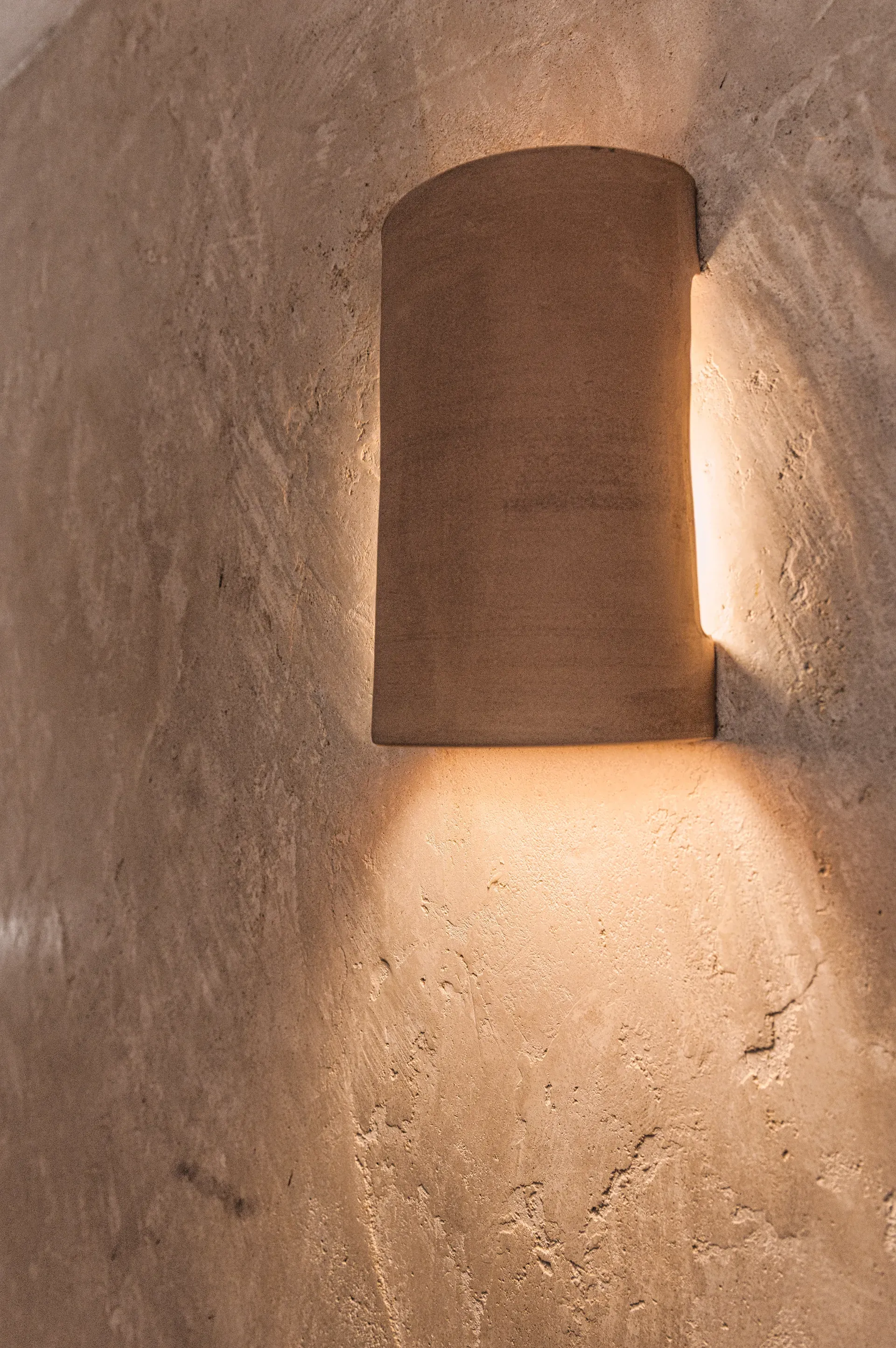 Aplique de pared curvo de terracota proyectando luz cálida sobre la textura vibrante del tadelakt