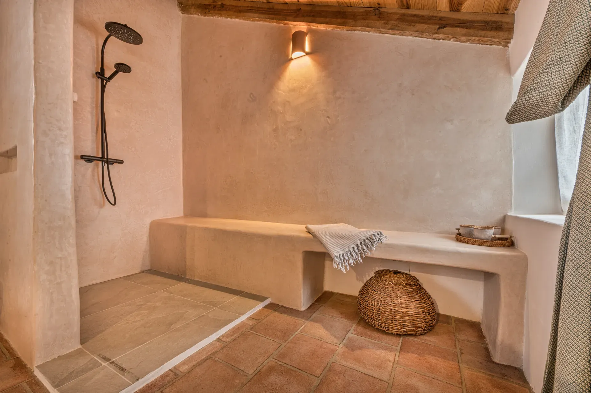 Ducha de obra en tadelakt bajo techo de madera, con banco integrado e iluminación cálida que realza los materiales naturales