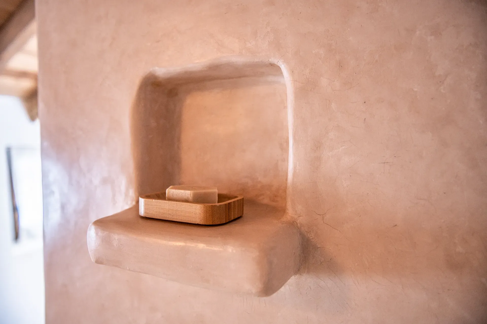 Hornacina perimetral moldeada en tadelakt con jabonera de madera y jabón natural sobre repisa continua