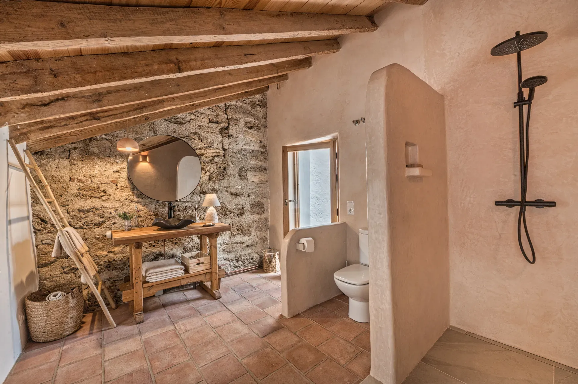Baño completo con ducha de tadelakt, muro de piedra vista y vigas de madera restauradas