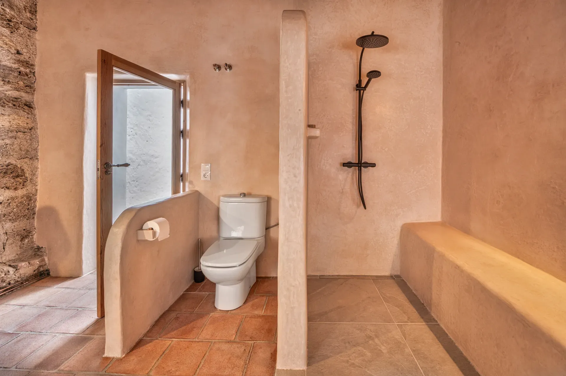 Zona de inodoro y ducha separadas por tabique curvo de tadelakt en ambiente de tonos tierra