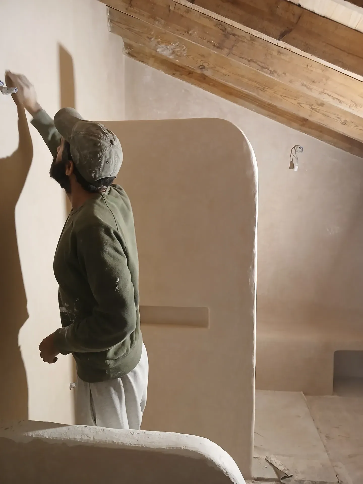 Artesano aplicando tadelakt en pared de ducha con tabique curvo y techo inclinado de madera