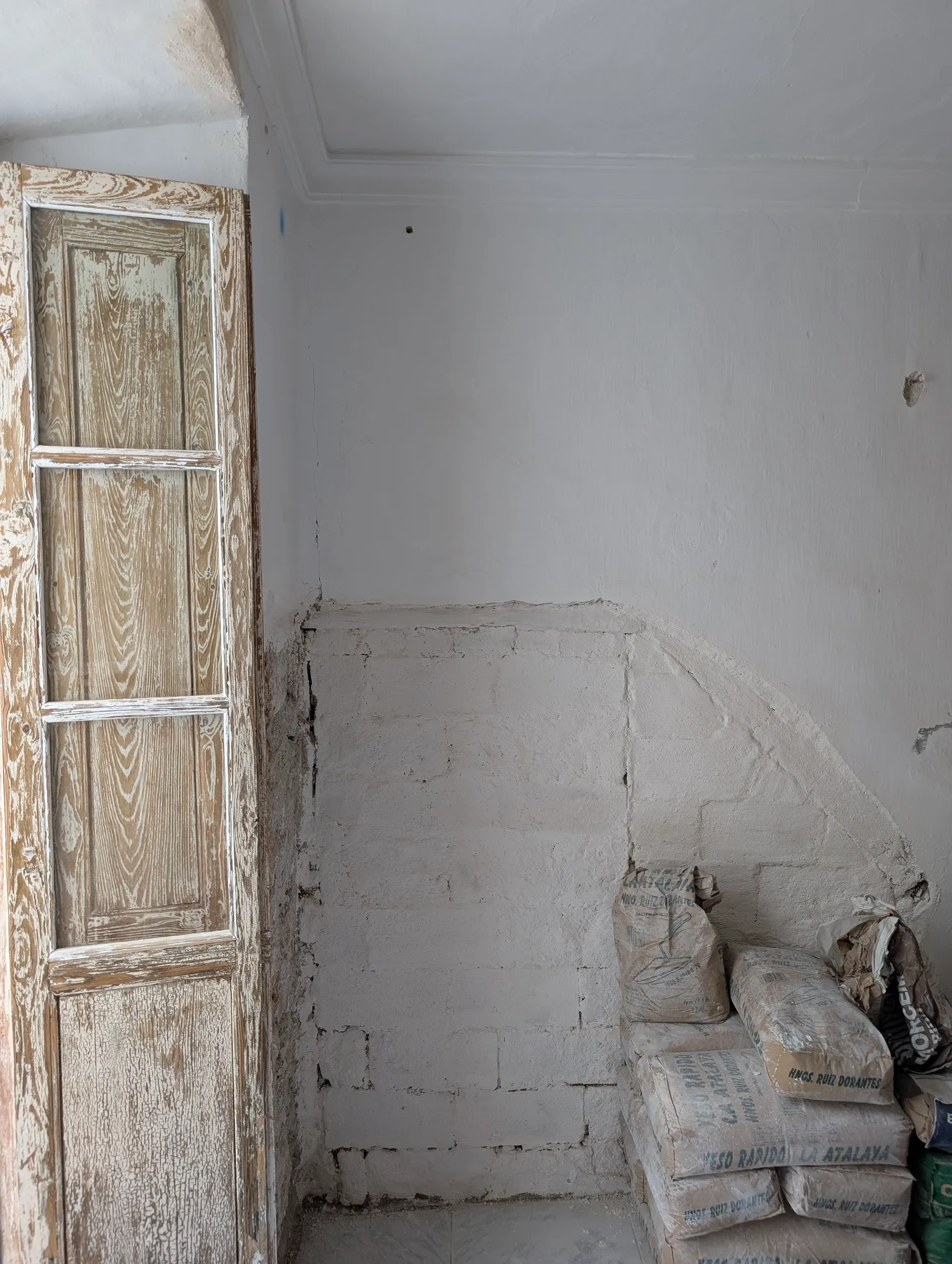 Detalle de puerta de madera antigua recuperada junto a muro saneado con mortero de cal y sacos de material