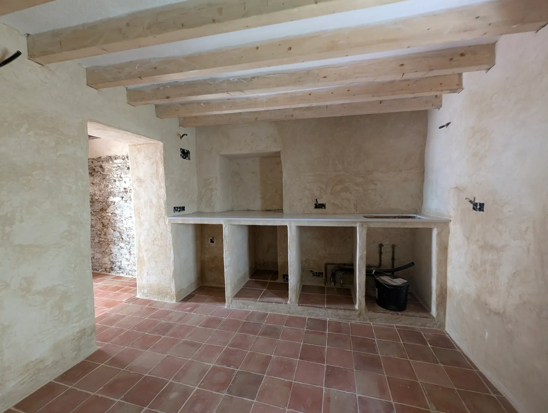 Cocina de obra con acabados continuos de trabadillo y techo de vigas de madera, integrando muros de piedra existentes