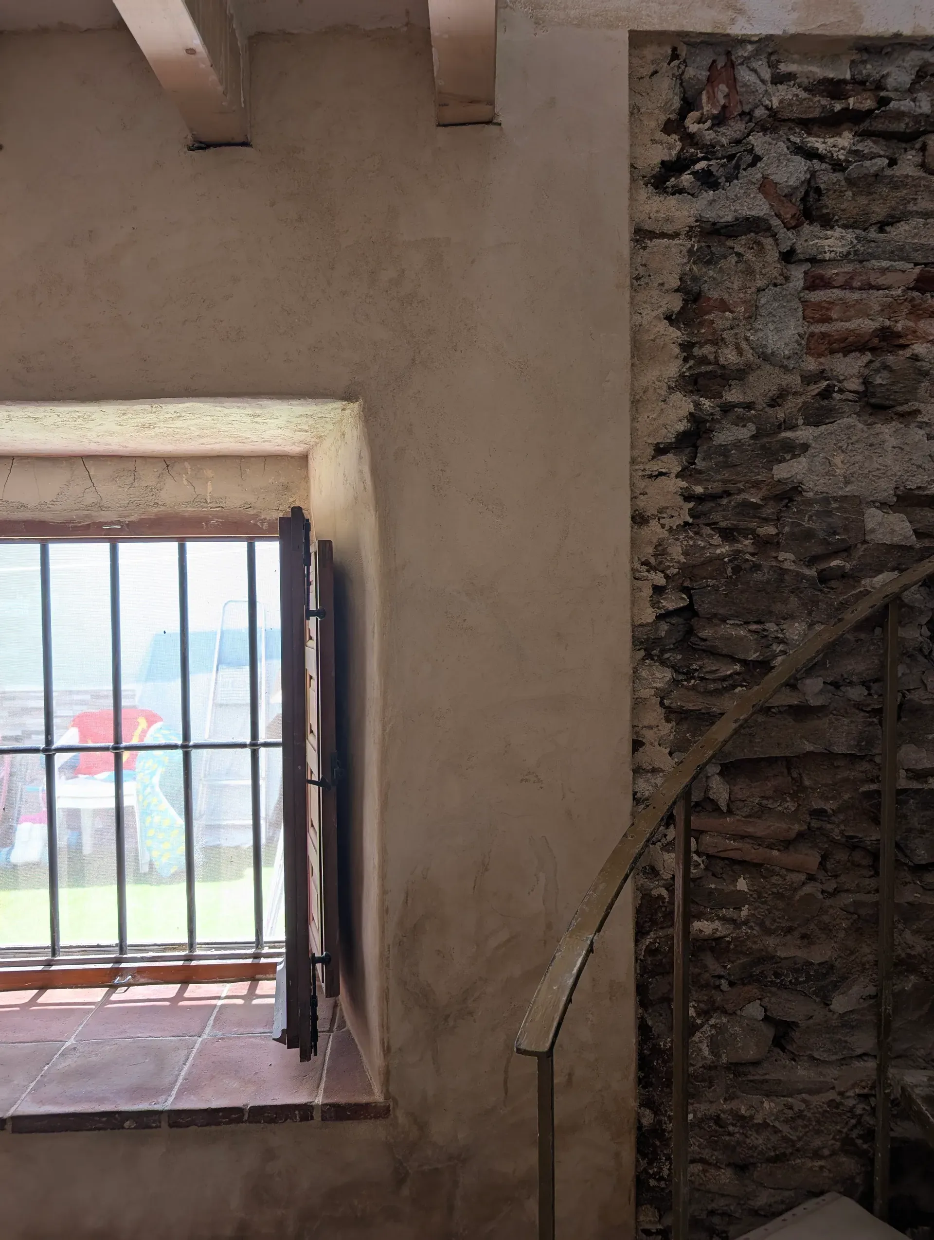 Ventana con contraventanas de madera en muro de gran espesor, junto a escalera de caracol y paramento de piedra vista